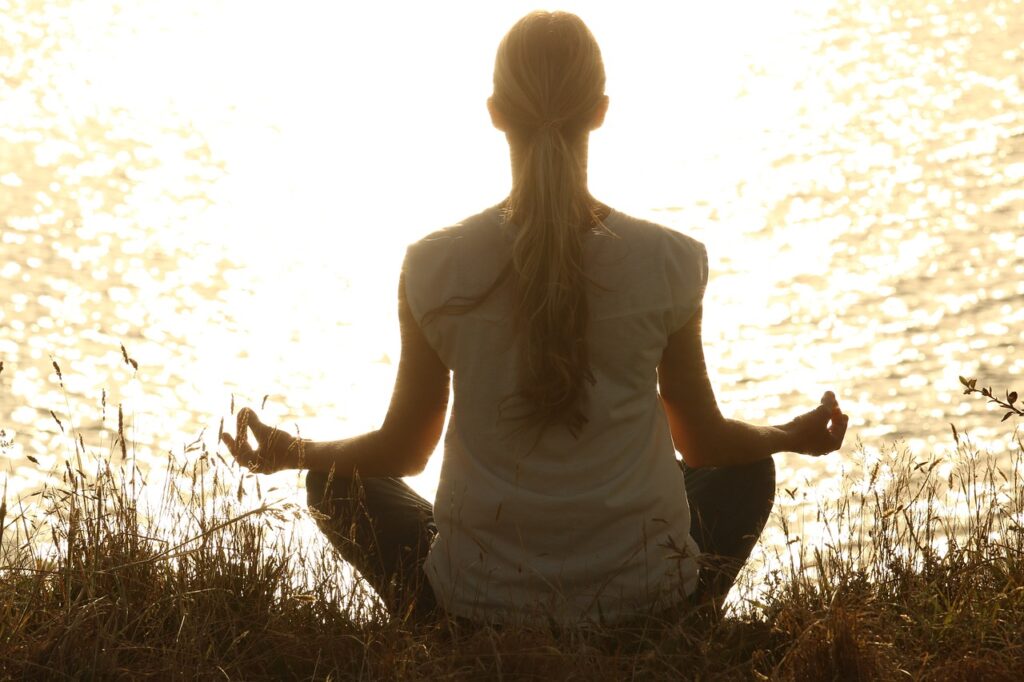 A woman practicing yoga at sunset, seen from behind, in a relaxed pose promoting mindfulness and relaxation.