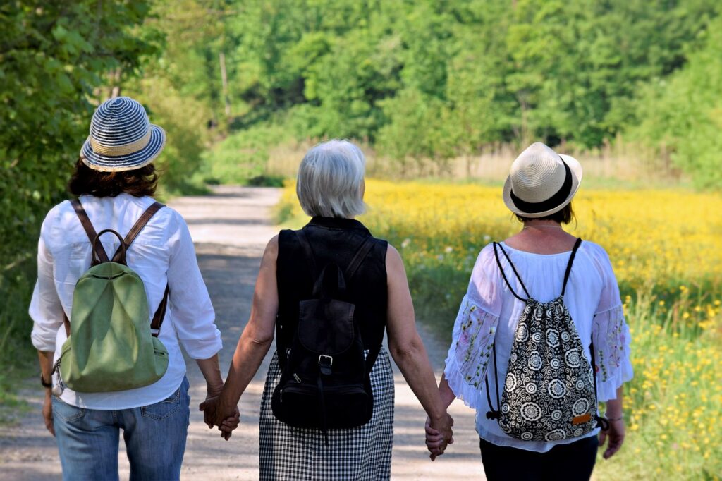 Three elderly women walking on a path through nature, seen from behind, showcasing friendship and enjoying a hike together.